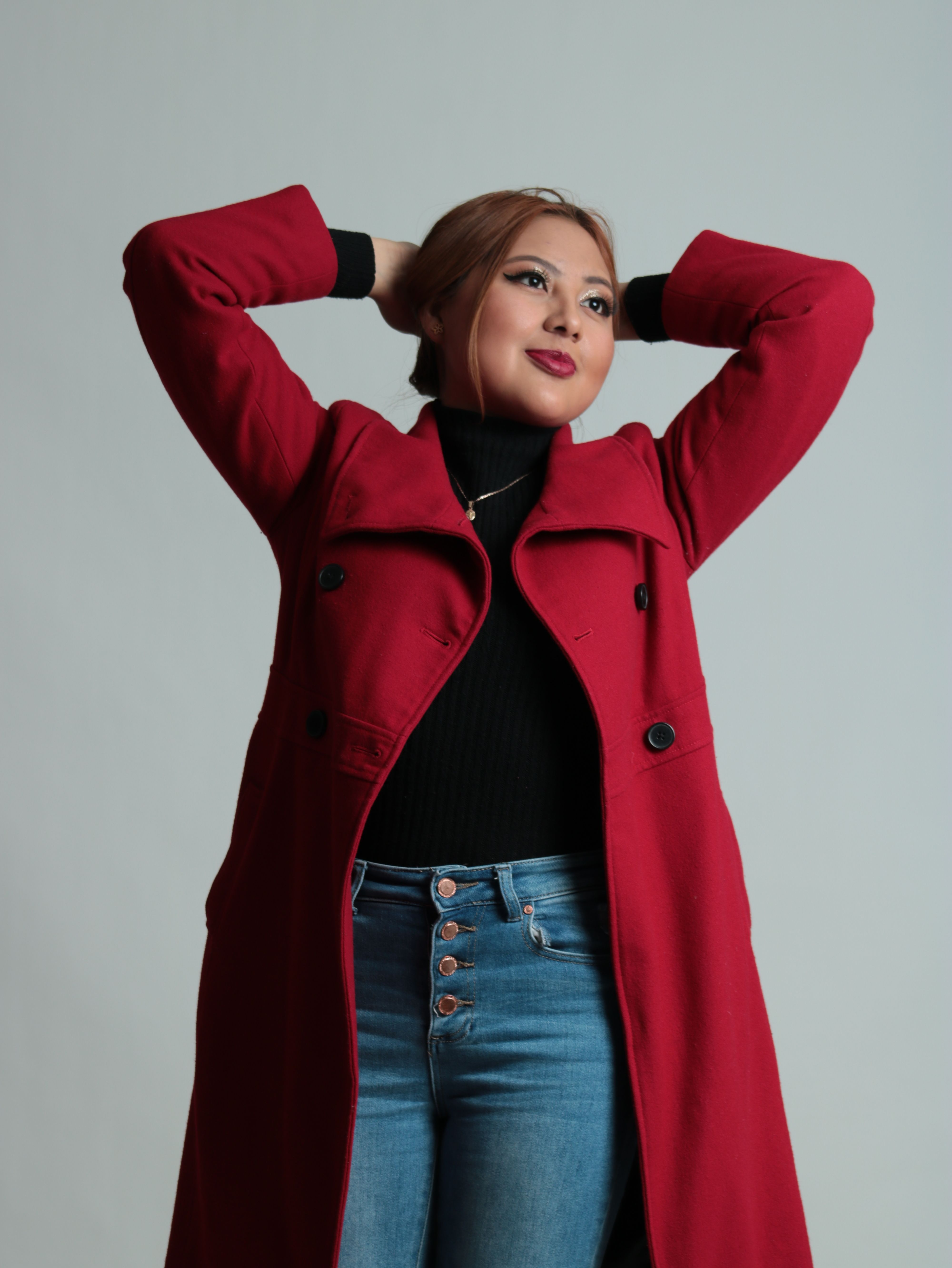 Elegant woman posing confidently in a red coat against a gray background.
