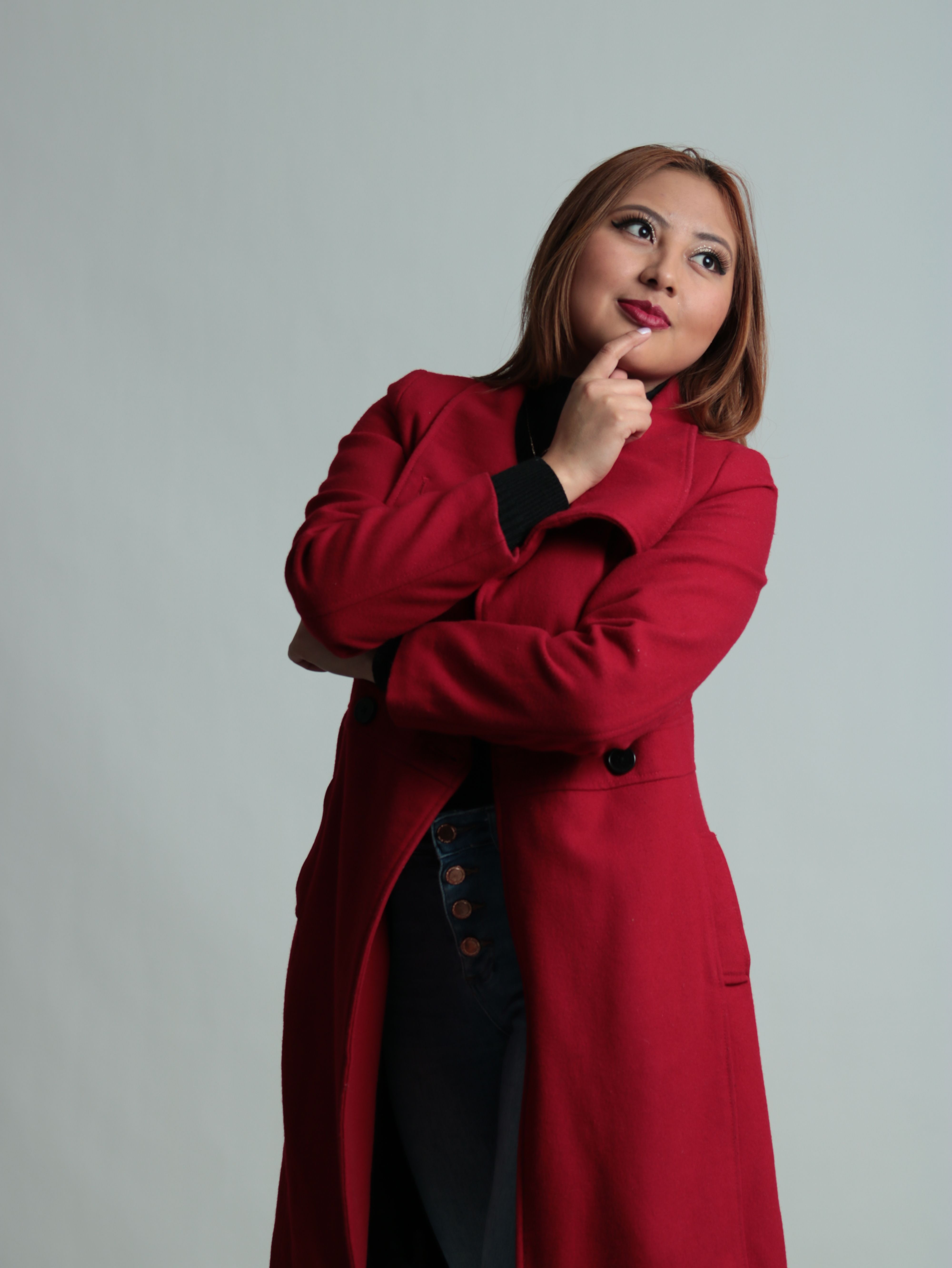 Woman in a red coat posing in a studio setting, thoughtful expression.