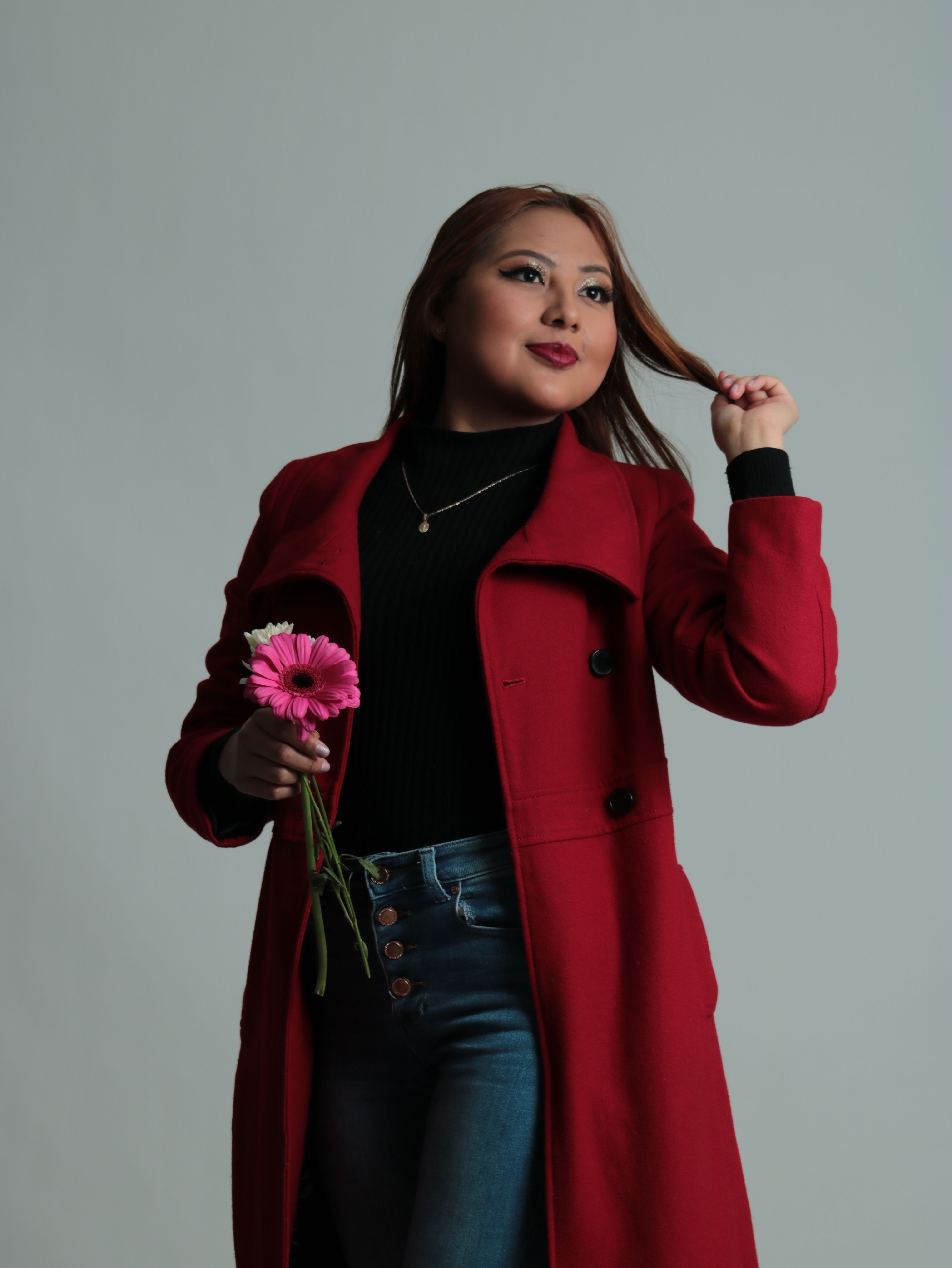 Fashionable woman in a red coat holding flowers, posing in studio.
