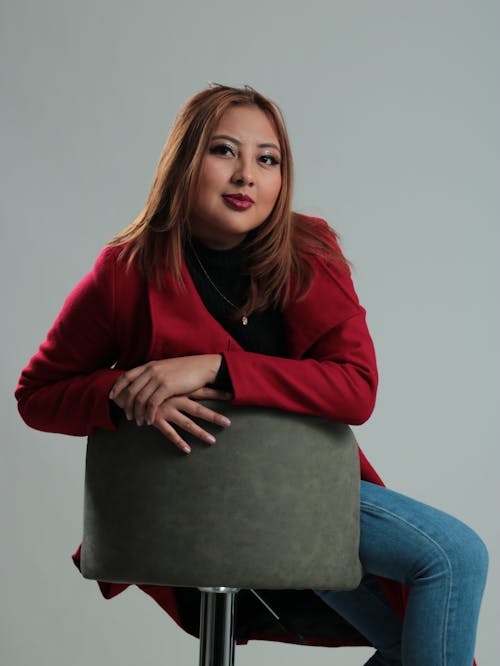 A woman sitting on a stool in a red coat