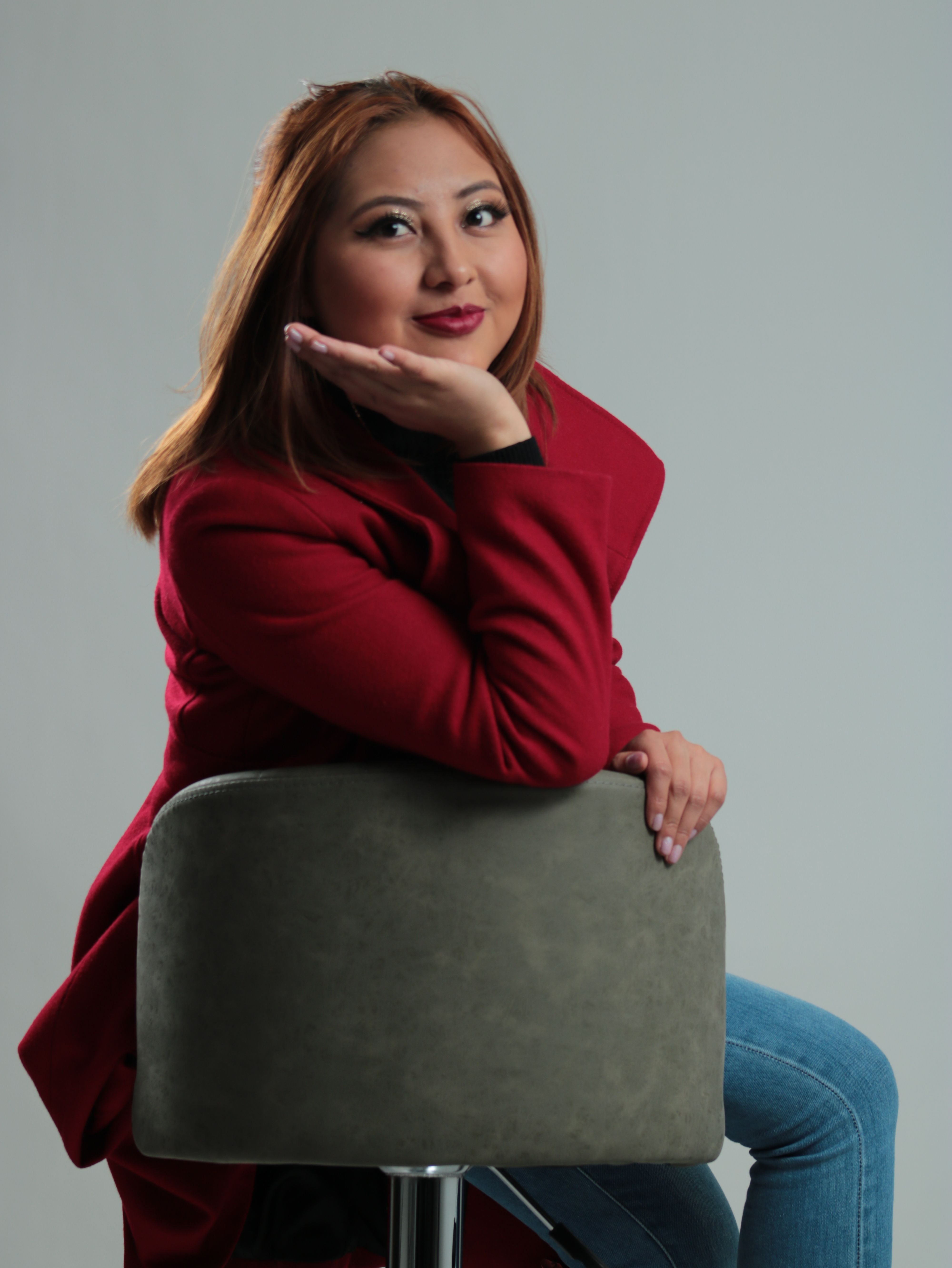 Studio portrait of a woman in a stylish red coat sitting on a chair, exhibiting elegance.