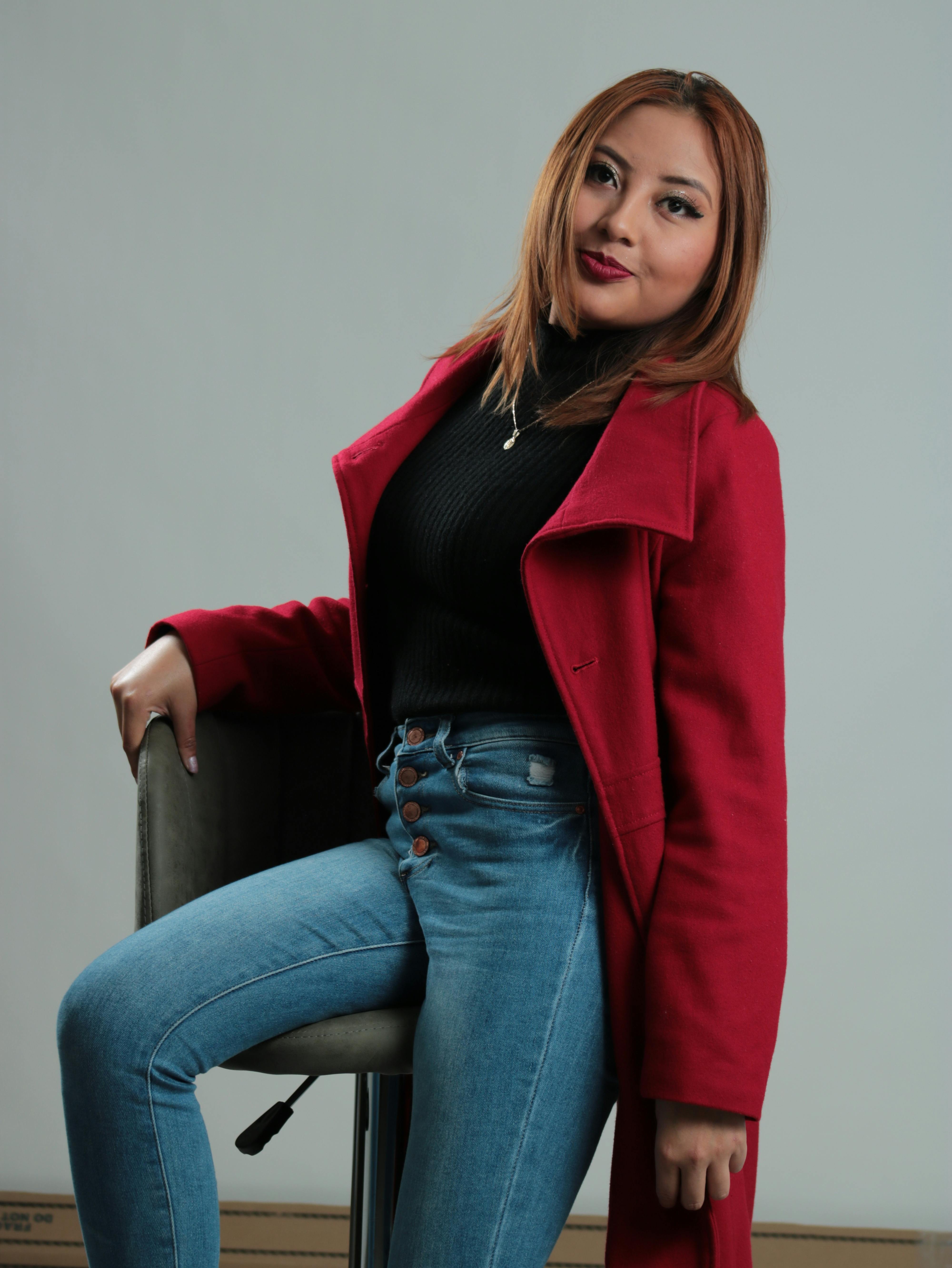 Fashion portrait of a woman in a red coat sitting confidently on a stool, showcasing modern style.