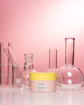 Beauty cream surrounded by laboratory glassware on a stylish pink backdrop.