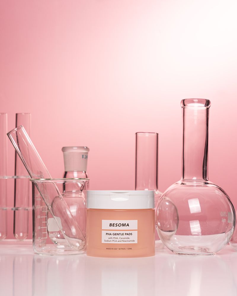 Cosmetic cream bottle beside scientific laboratory glassware on pink background