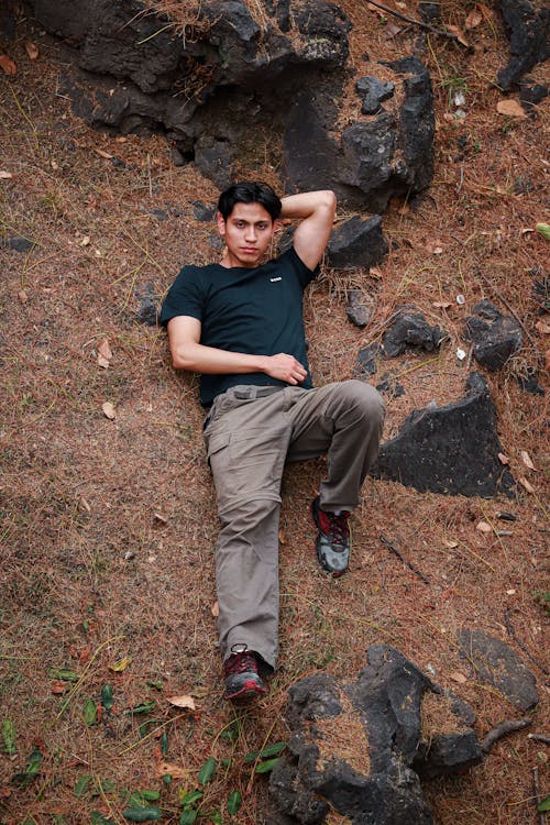 Brunette Man in T-shirt Lying Down among Rocks on Ground