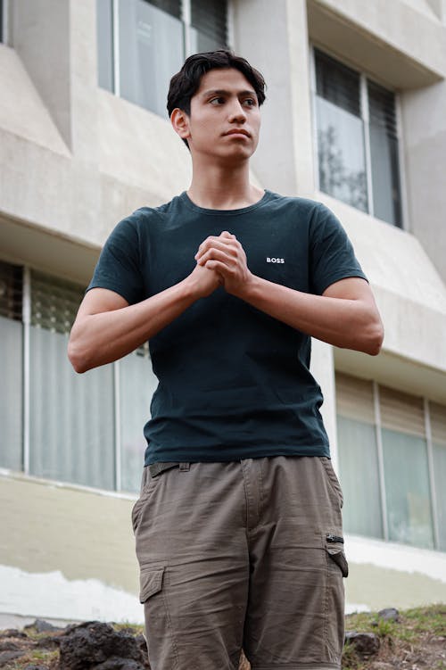 A man in a green shirt and khaki pants is standing in front of a building