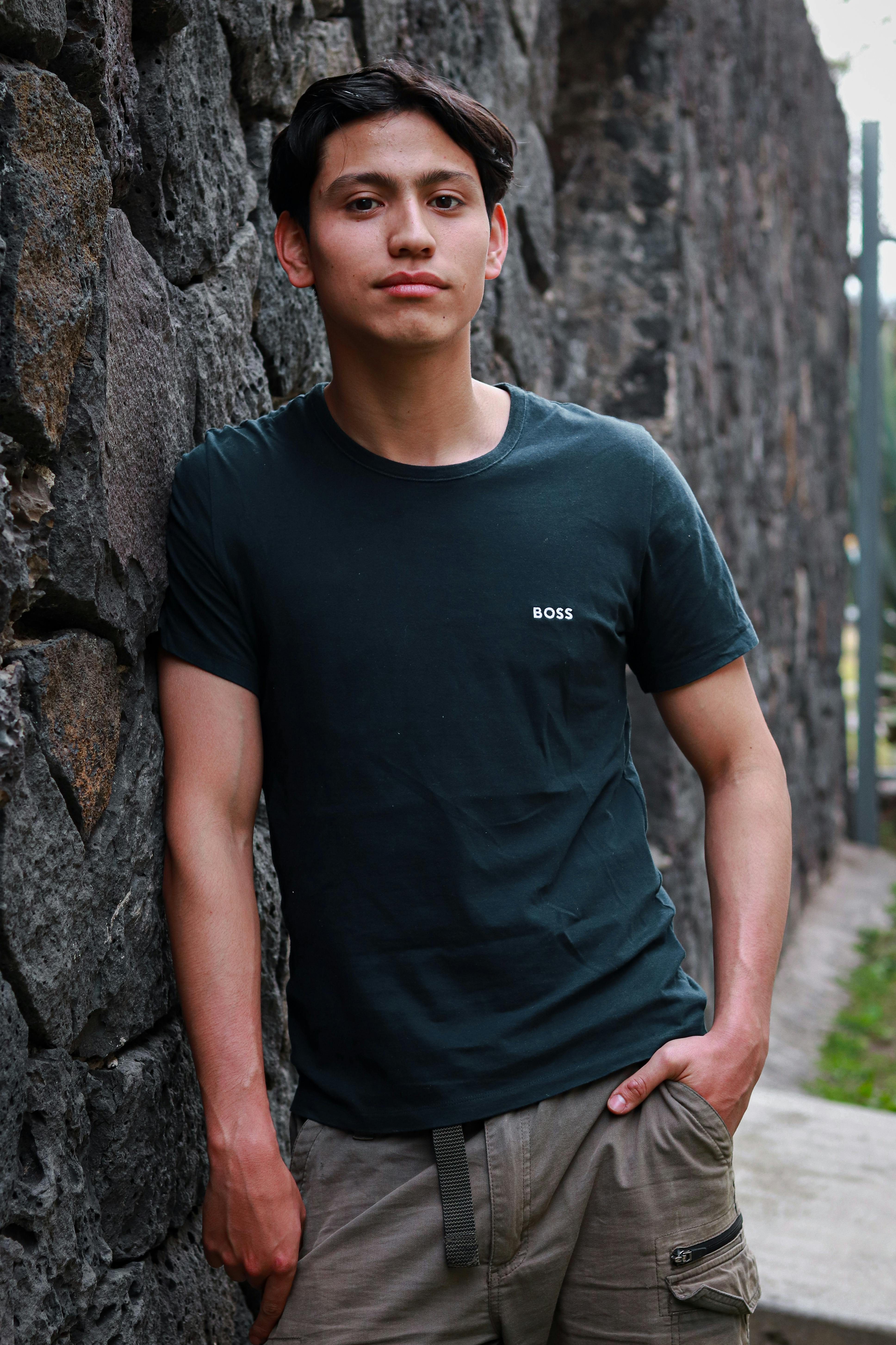 Fashionable young man in a black t-shirt poses against a textured stone wall in Ciudad de México, CDMX.