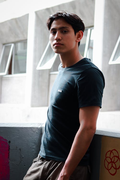 A young man in a black t - shirt standing next to a wall