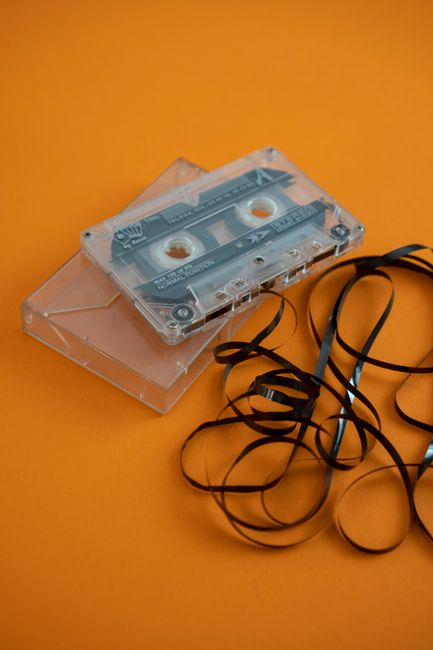 A vintage audio cassette with tangled tape, captured against an orange backdrop, evoking retro nostalgia.