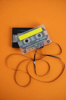 Vintage audio cassette with unraveled tape on vibrant orange background.