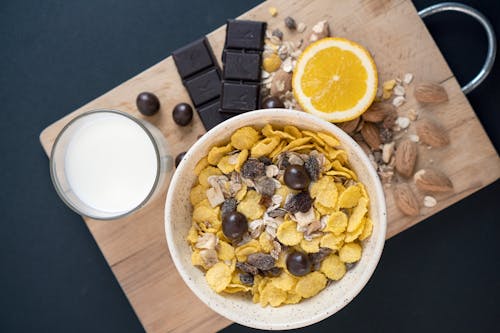 A bowl of cereal with nuts, chocolate and orange slices