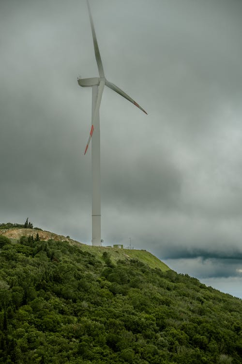 A wind turbine on a hill with cloudy skies