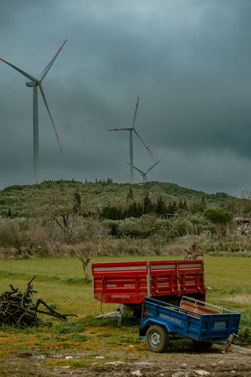 A red truck and a blue cart are parked in front of wind turbines