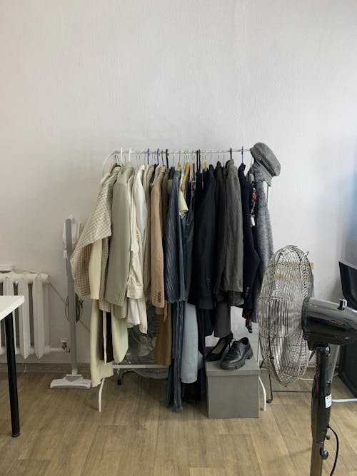 A rack of clothes in a room with a fan