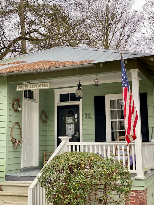 A small green house with an american flag on the porch