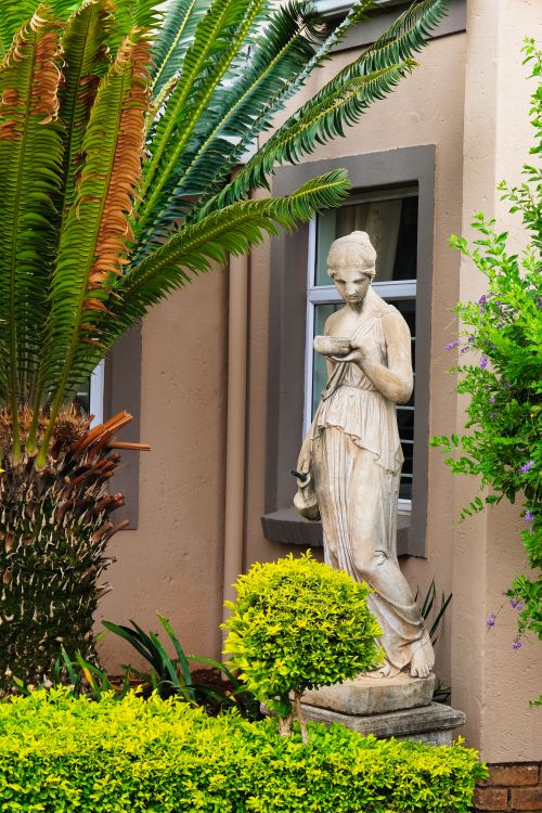 Free Elegant stone statue amidst vibrant greenery and palm trees in Pretoria, South Africa. Stock Photo