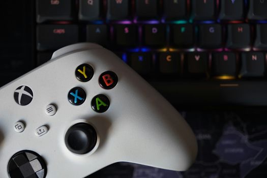 Game controller beside illuminated RGB keyboard, highlighting technology and gaming equipment.