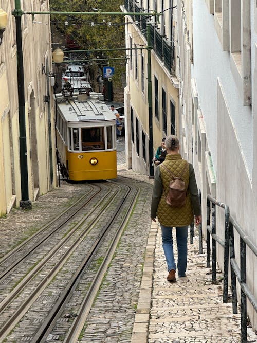 A person walking down a narrow street with a yellow tram