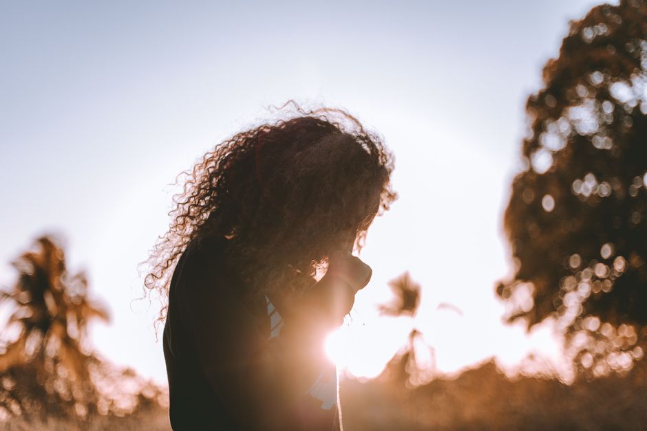 A serene silhouette of a woman under the setting sun, capturing a peaceful moment outdoors.