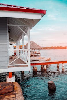 Scenic view of a beach house on stilts over the ocean with a vibrant sunset in the background.