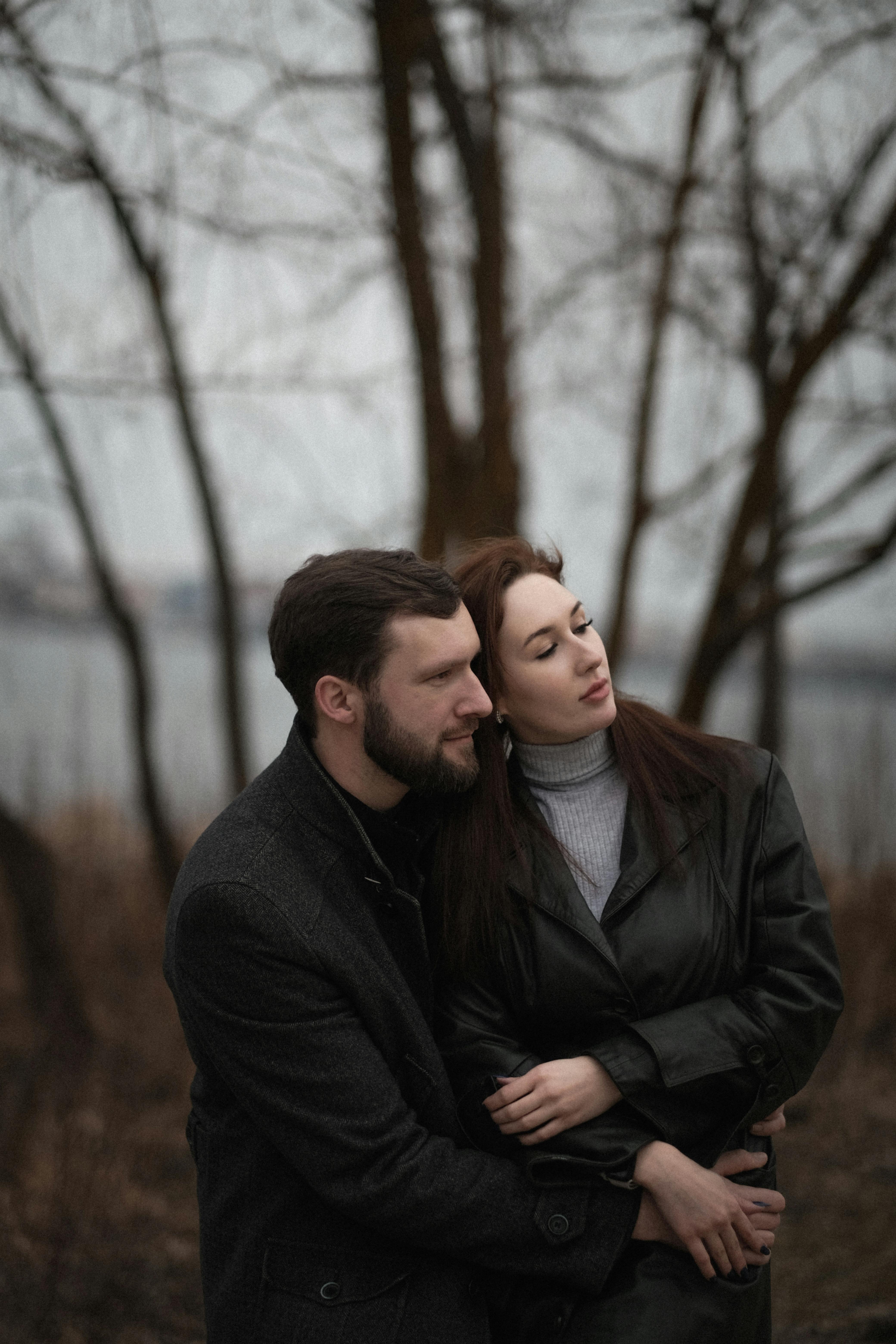 A couple embracing in a moody autumn scene with bare trees.