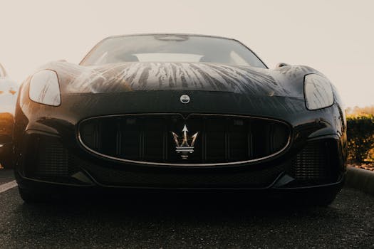 Front view of a sleek black Maserati with raindrops on the hood in a parking lot.