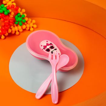 Bright pink kids tableware set with fork and spoon on an orange background.（イメージ）