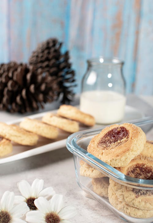 A glass container with cookies and milk on a table