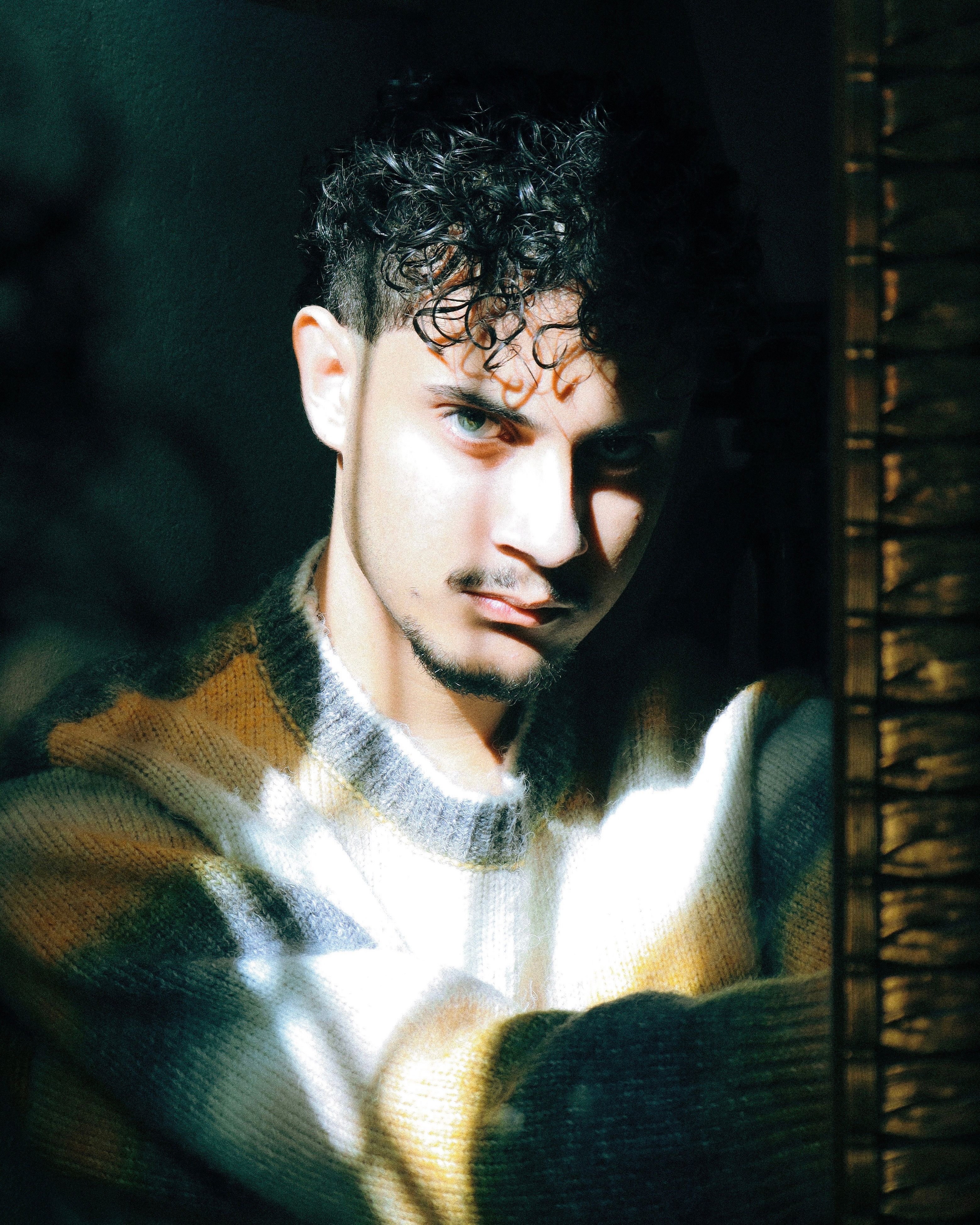 Artistic portrait of a man in a sweater with sunlight casting unique patterns.