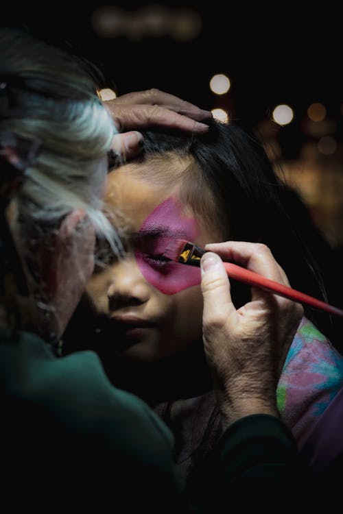 A woman is painting a child's face with a brush