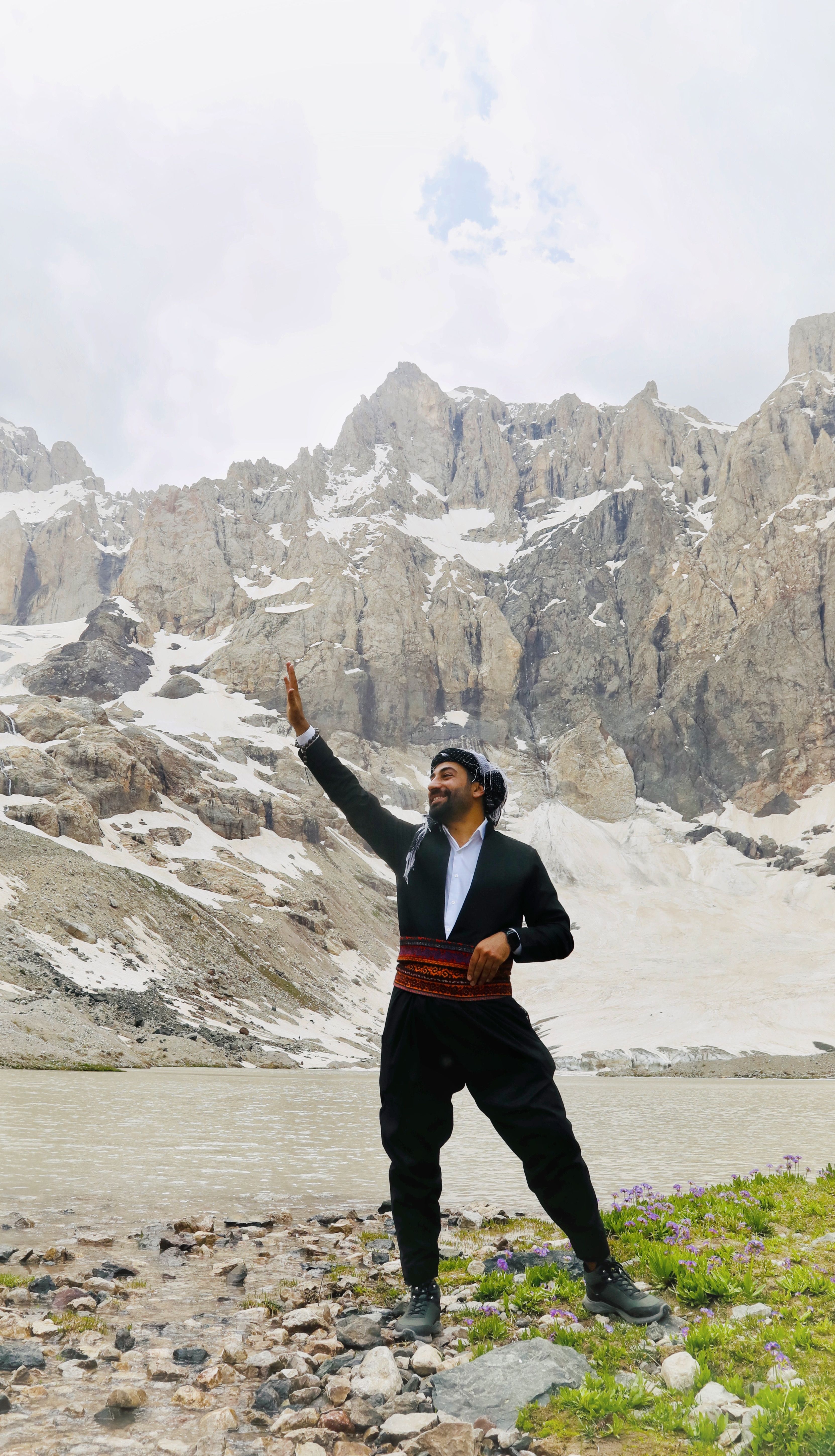 Man in traditional attire waving in the snowy mountains of Hakkari, Türkiye.