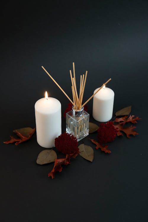 A candle, two sticks and some leaves on a black background
