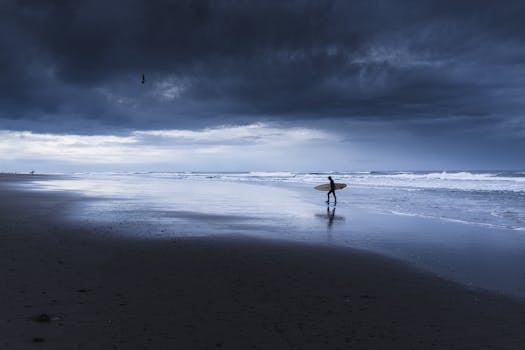 A lone surfer walks along Lincoln City's beach under dramatic storm clouds, ready to take on the ocean waves.