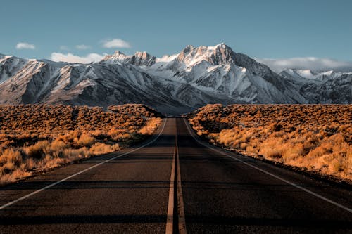 An empty road with snow capped mountains in the background