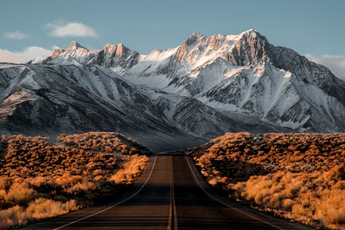 A long road with snow capped mountains in the background