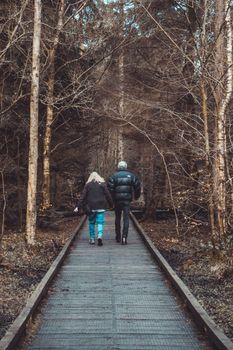 Senior couple walking together on a wooden trail through autumn forest.