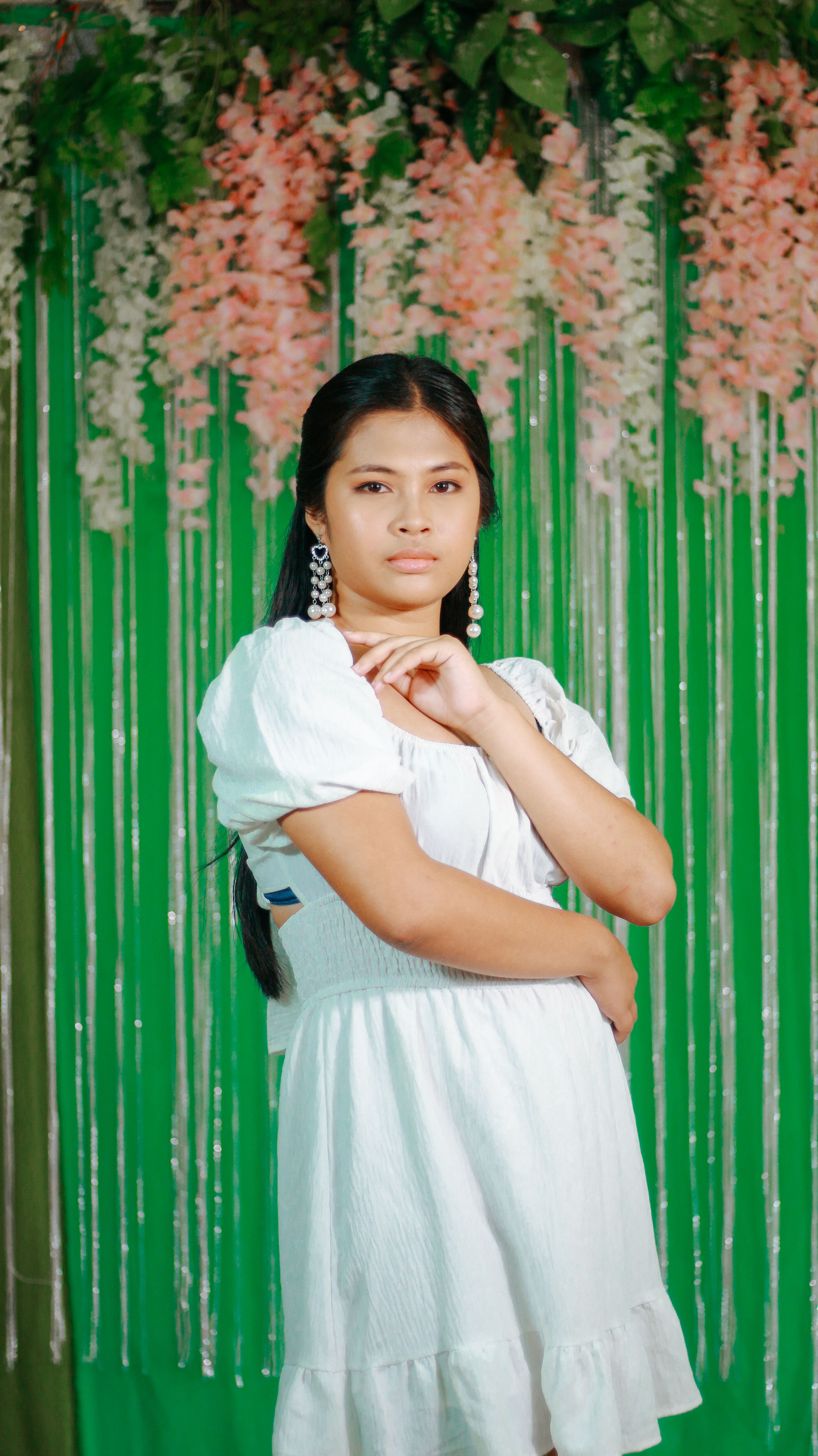Stylish portrait of an Asian woman in a white dress with a floral background.
