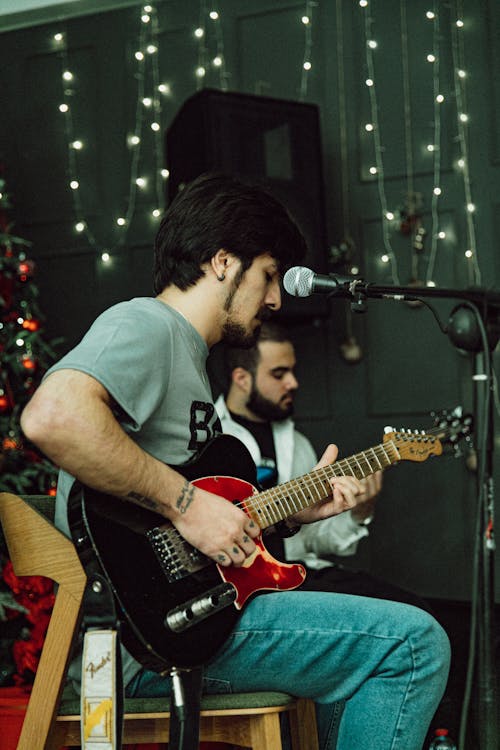 A man playing guitar in front of a christmas tree