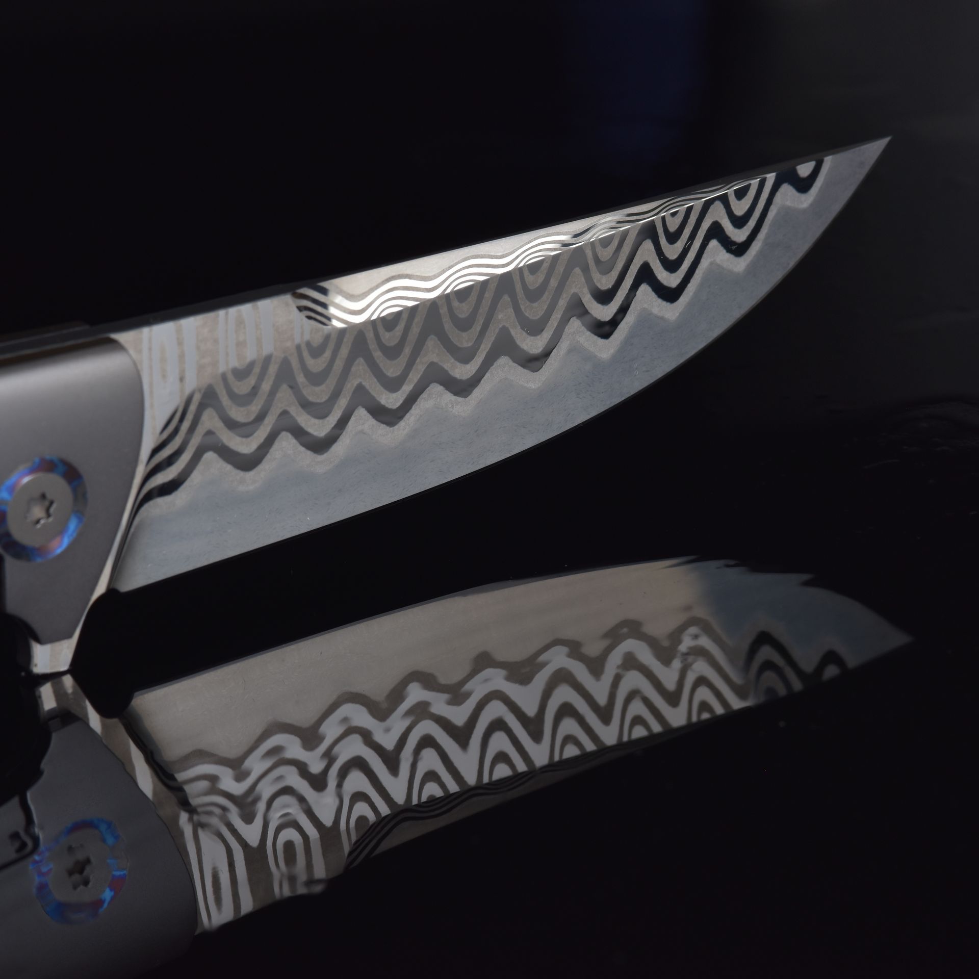 Close-up of a Damascus steel knife blade with intricate wave patterns on a black background