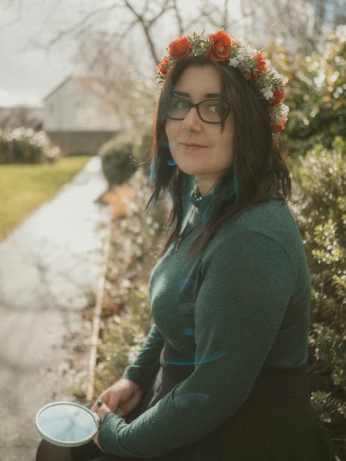 A woman wearing glasses and a flower crown sitting on a bench