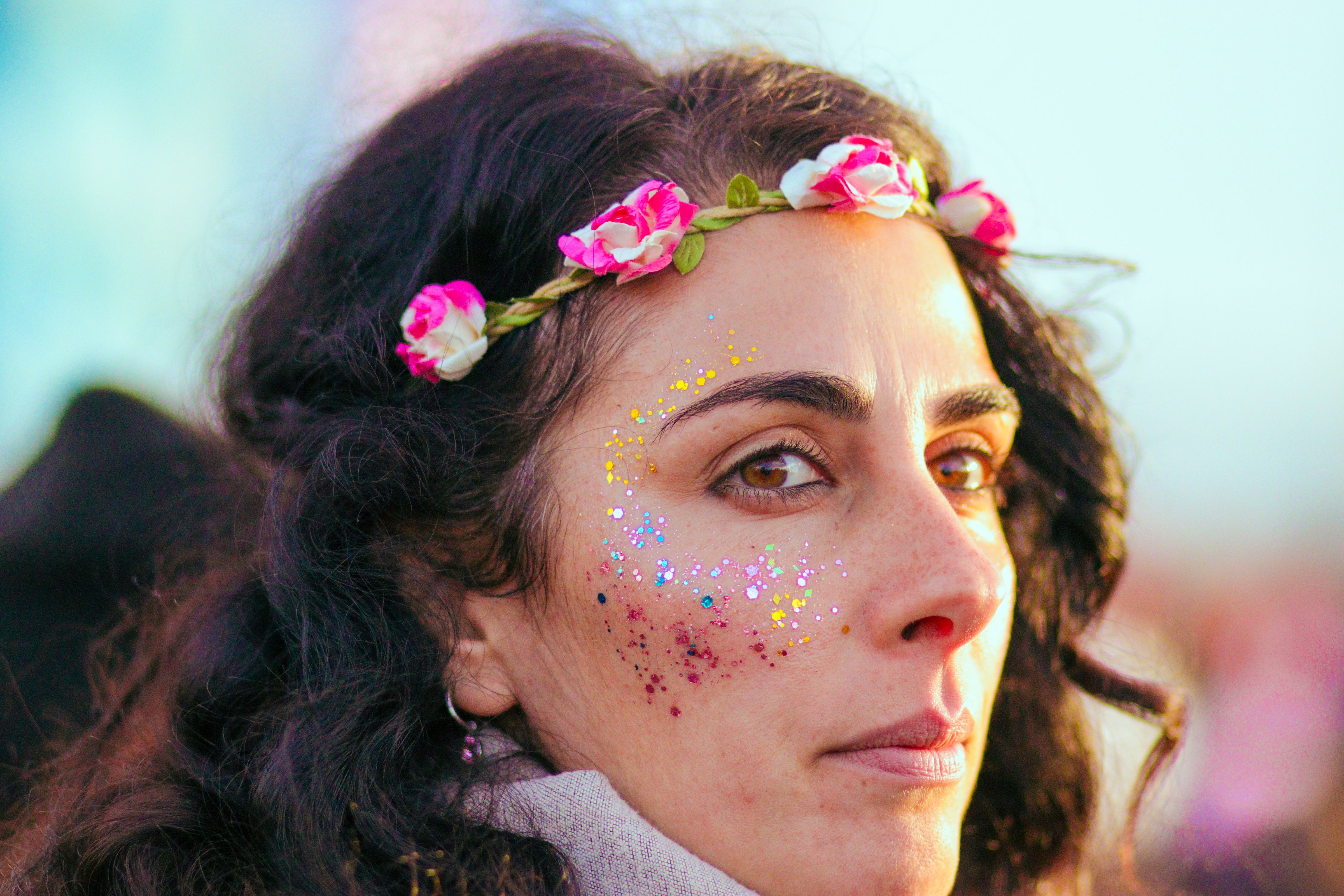 Portrait of a woman with creative makeup and floral headband in sunlight at a festival.
