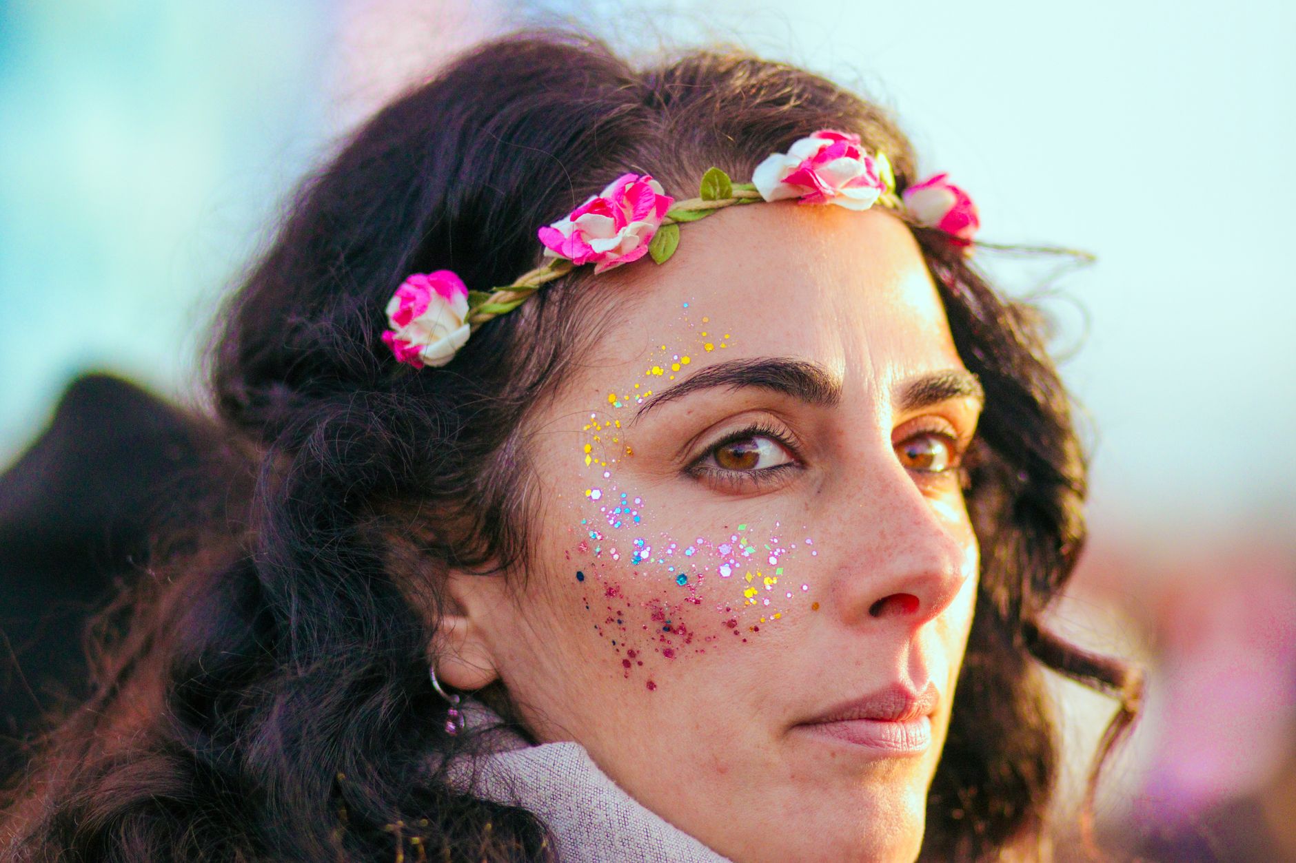 Portrait of a woman with creative makeup and floral headband in sunlight at a festival.