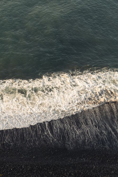 Free A stunning aerial view capturing ocean waves crashing onto a pebble beach, showcasing nature's power. Stock Photo