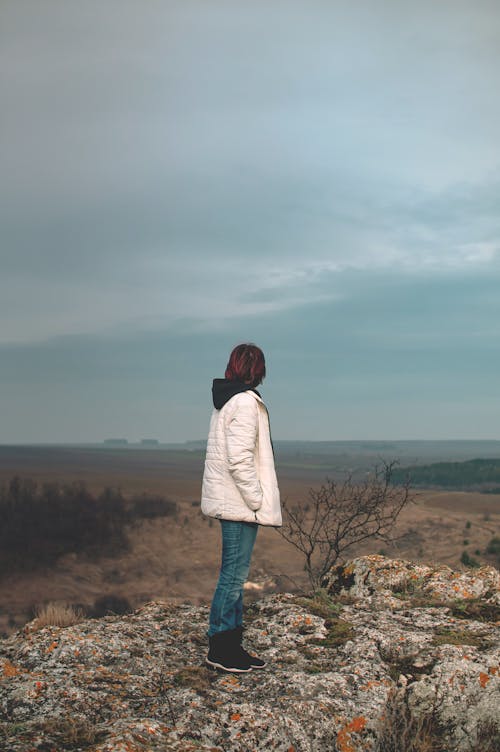 A Woman in a Jacket Standing on a Rocky Hill 