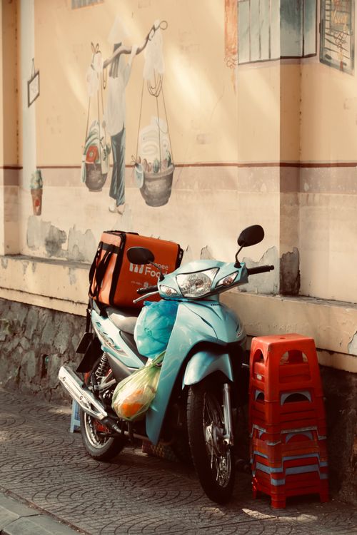 Free Blue scooter with delivery box against mural wall in city street, showcasing urban life. Stock Photo
