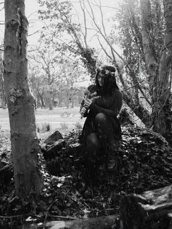A black and white photo of a woman sitting in the woods