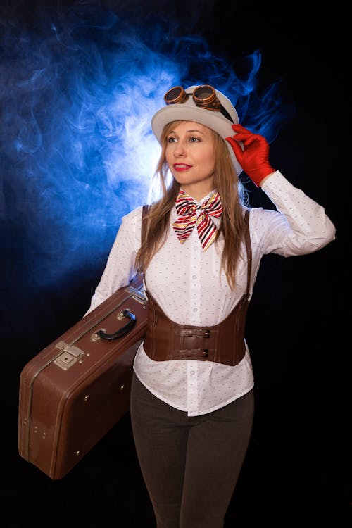 A woman in a hat and bow tie holding a suitcase