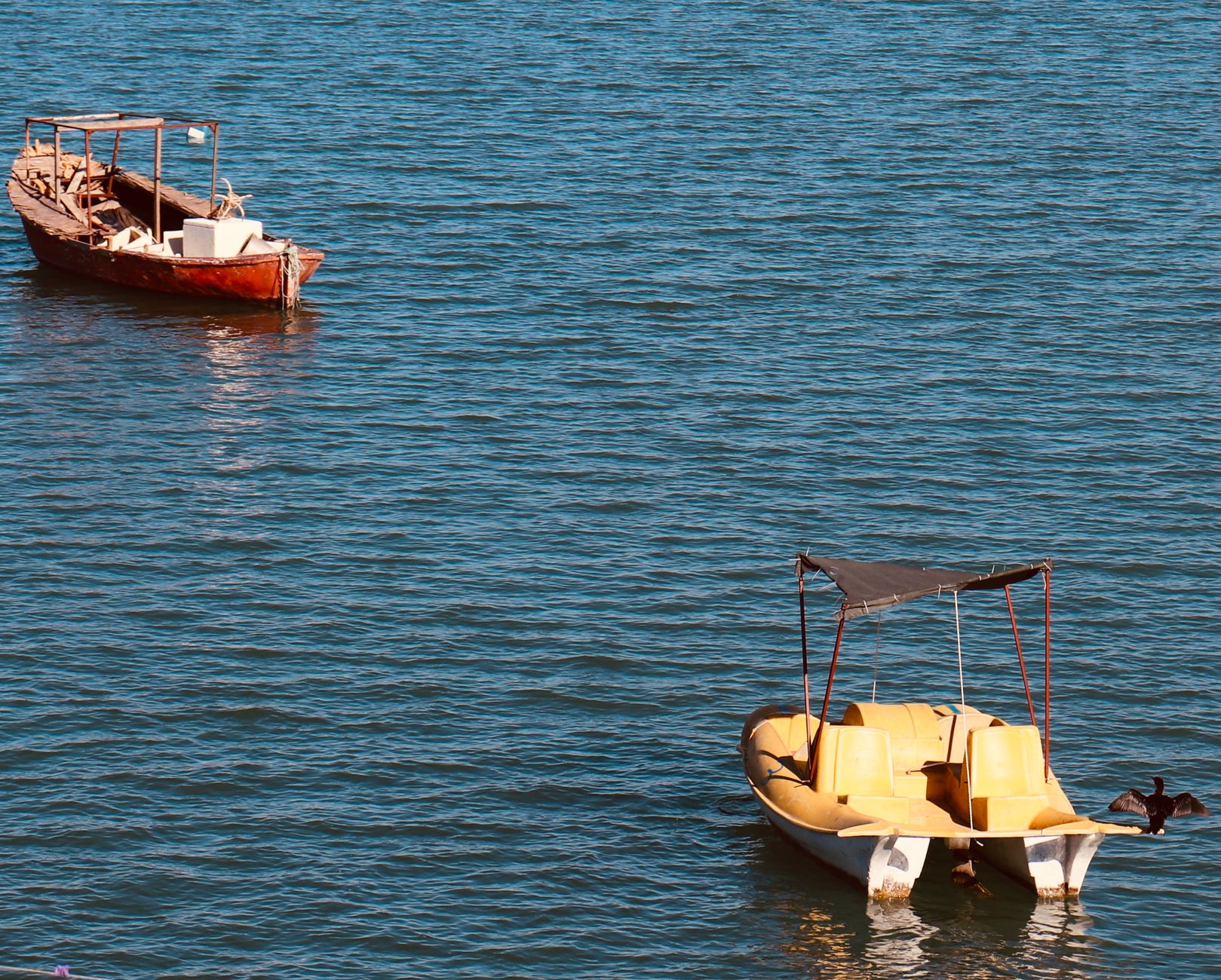 Two wooden boats floating peacefully on calm blue water under a sunny sky.
