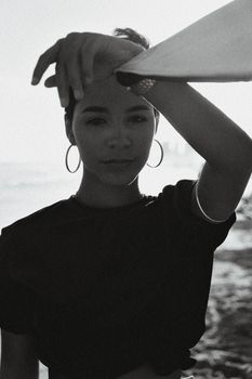 Artistic black and white portrait of a woman at the beach, posing with hand raised.