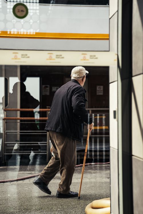 Free Senior man walking with a cane in a modern indoor urban environment, reflection visible. Stock Photo